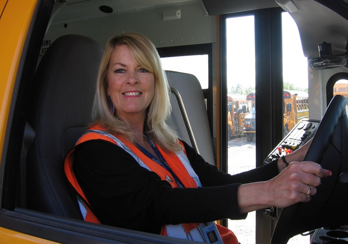 female-school-bus-driver-hands-on-wheel-smiling-for-camera